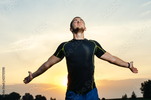 guy in sports clothing, standing looking into the sky . on the horizon the sunset. he spread his hands to meet the sun