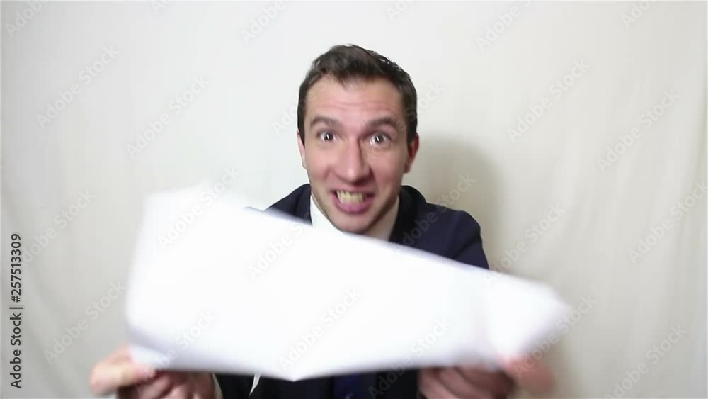 Young handsome businessman picks up a sheet with a contract, actively degenerates his displeasure, swears and throws out the contract. Portrait on a white background. Young handsome businessman picks up a sheet with a contract, actively degenerates his displeasure, swears and throws out the contract. Portrait on a white background.