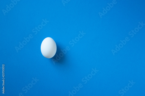 One single white egg on the bright blue background with space for text. White easter egg minimal composition. Easter clean blank.