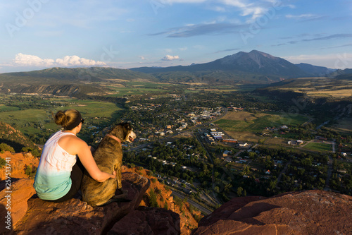 Young female and her dog overlooking a mountain and town at sunset photo