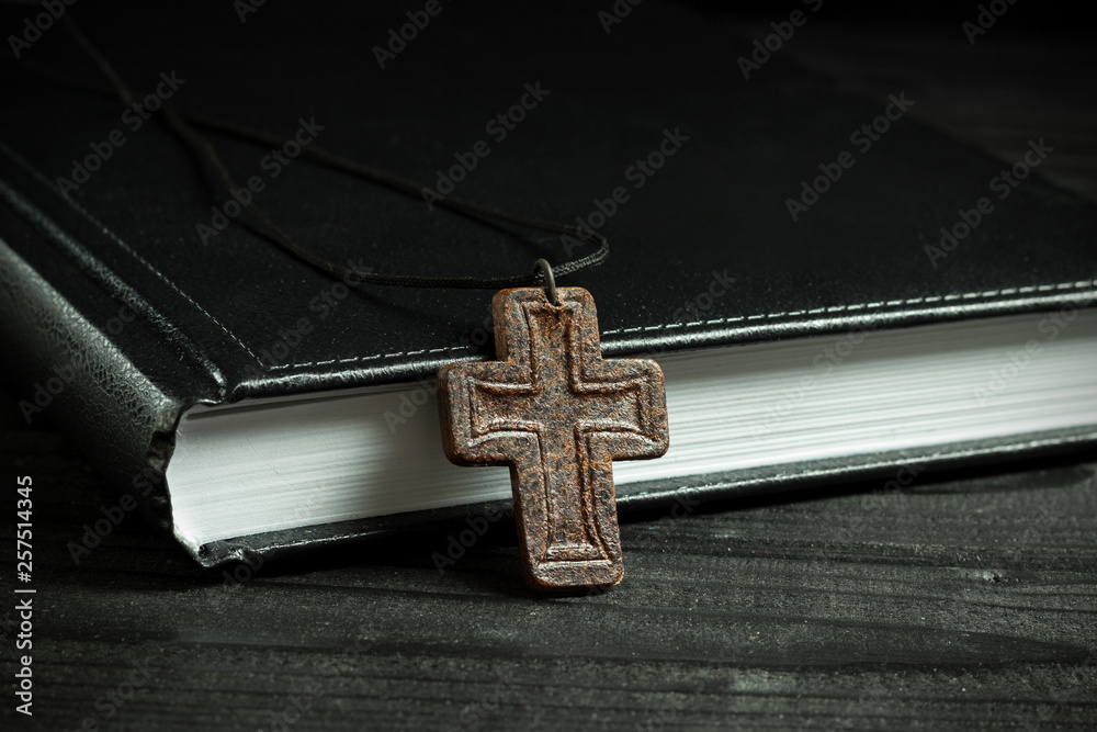 leather cross near the bible, on a wooden table in the dark