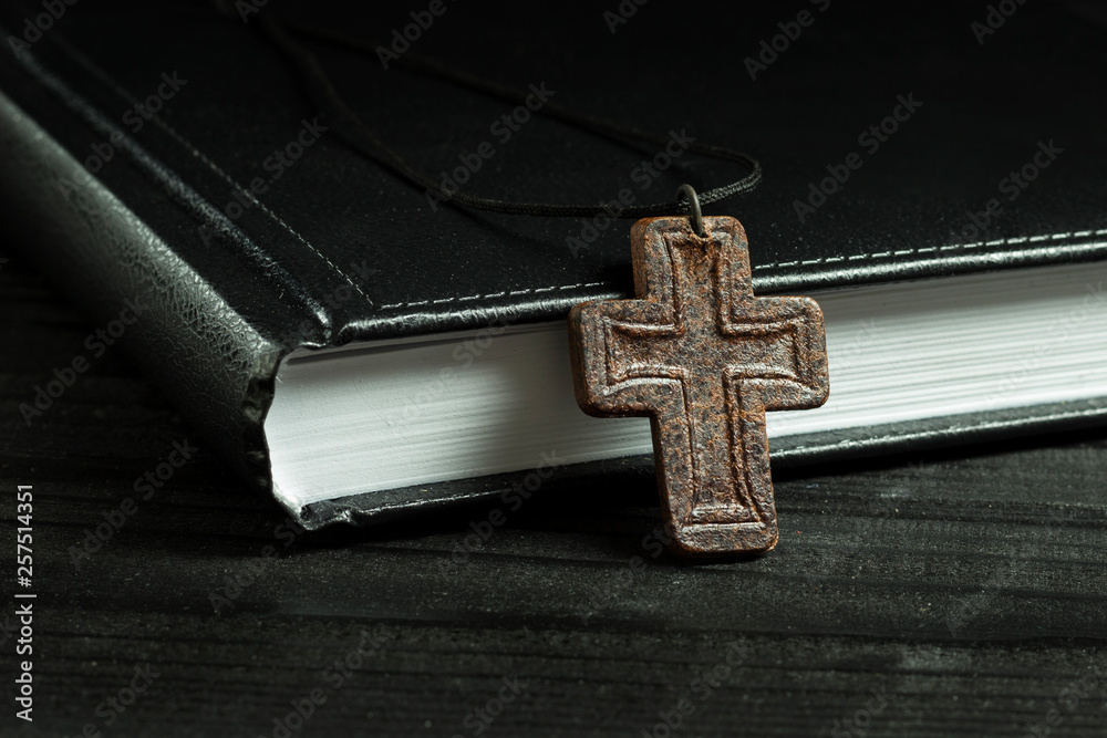 leather cross near the bible, on a wooden table, close-up