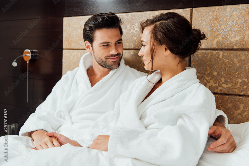 cheerful bearded man holding hands with beautiful girlfriend in bed