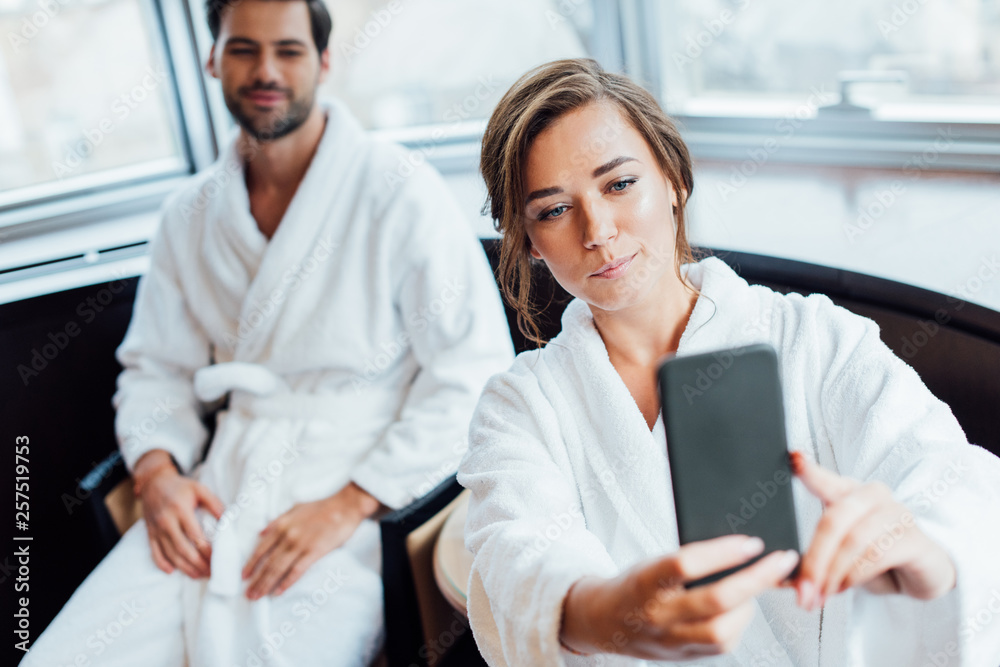 selective focus of attractive woman in bathrobe taking selfie with handsome boyfriend in hotel selective focus of attractive woman in bathrobe taking selfie with handsome boyfriend in hotel