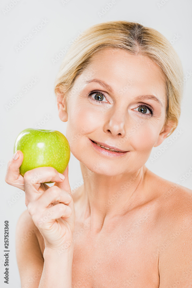 beautiful mature woman holding green apple and looking at camera on grey background beautiful mature woman holding green apple and looking at camera on grey background