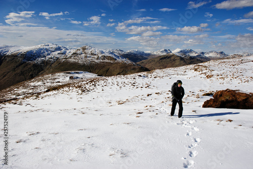 A female hiker climbing in a snowed steep slope with a mountain landscape bacground at The Loch Lomond & The Trossachs National Park, Scotland, UK.