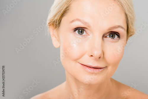 attractive and blonde mature woman looking at camera isolated on grey