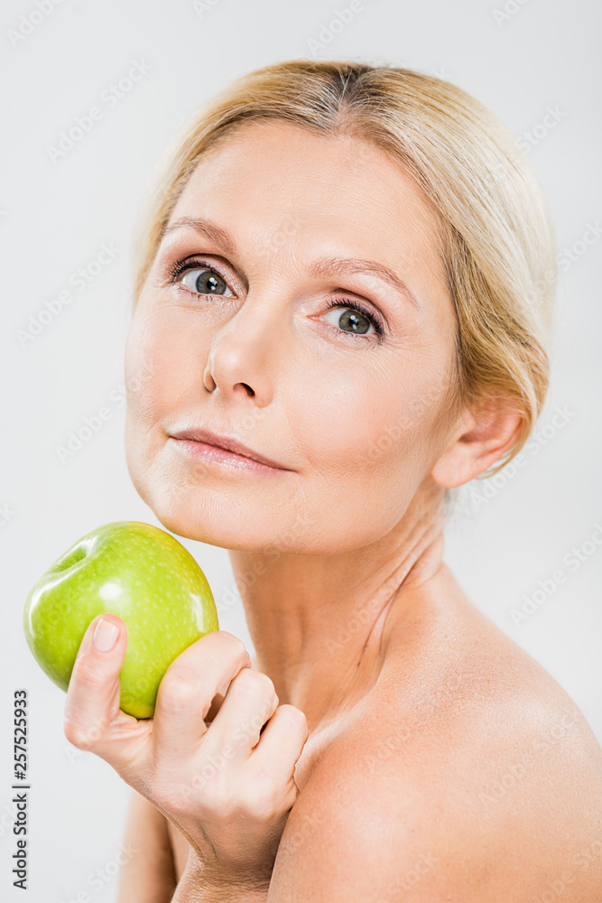 beautiful and mature woman holding green ripe apple and looking at camera isolated on grey beautiful and mature woman holding green ripe apple and looking at camera isolated on grey