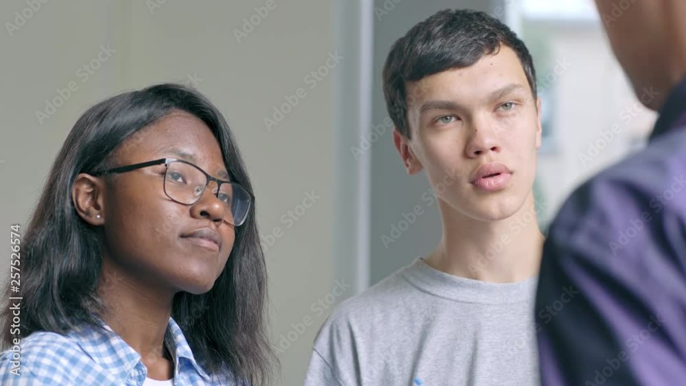 Two diverse students, African girl and Asian boy asking questions to teacher drawing graphs on whiteboard and listening to him attentively Two diverse students, African girl and Asian boy asking questions to teacher drawing graphs on whiteboard and listening to him attentively