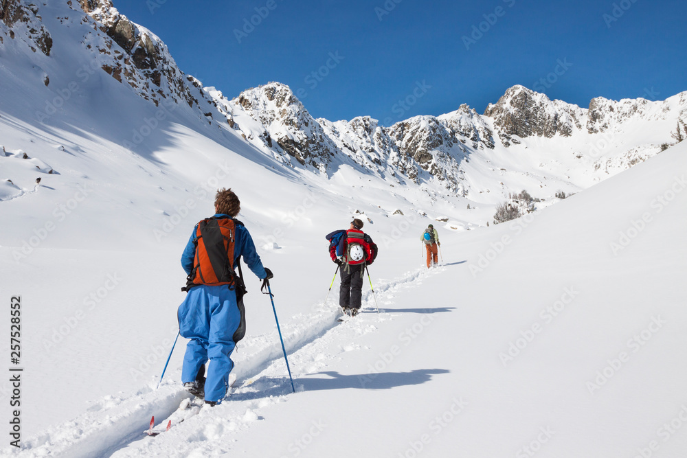 Three fit male backcountry skiers with backpacks on skin in a valley in the Beehive Basin near Big Sky, Montana. Three fit male backcountry skiers with backpacks on skin in a valley in the Beehive Basin near Big Sky, Montana.