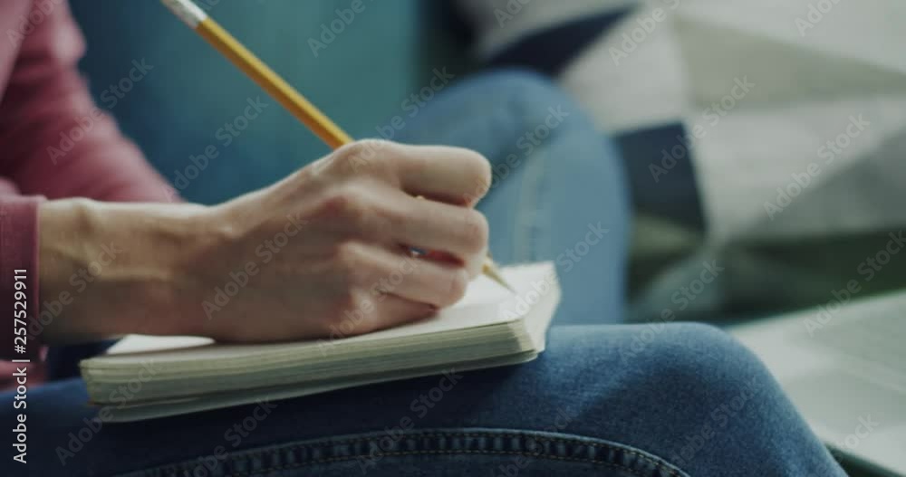 Close up of the notebook on the knees of the woman while she writing down notes with a pencil in it.