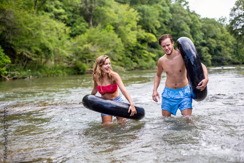 Young couple walking down river with tubes