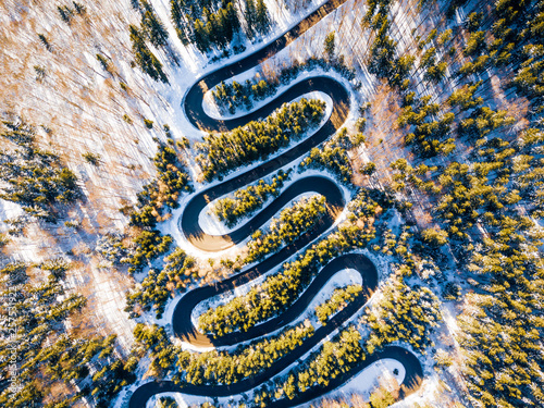 Winding road through the forest, from high mountain pass, in winter time. Aerial view by drone . Romania
