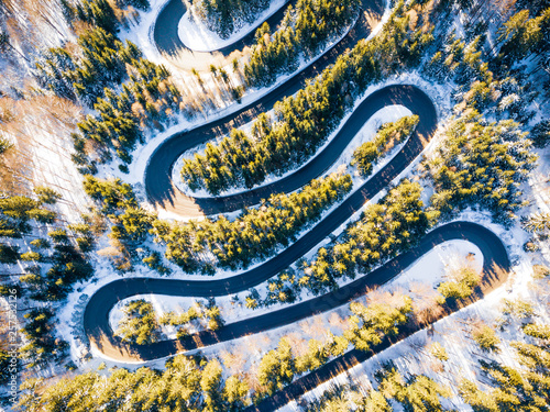 Winding road through the forest  from high mountain pass  in winter time. Aerial view by drone . Romania