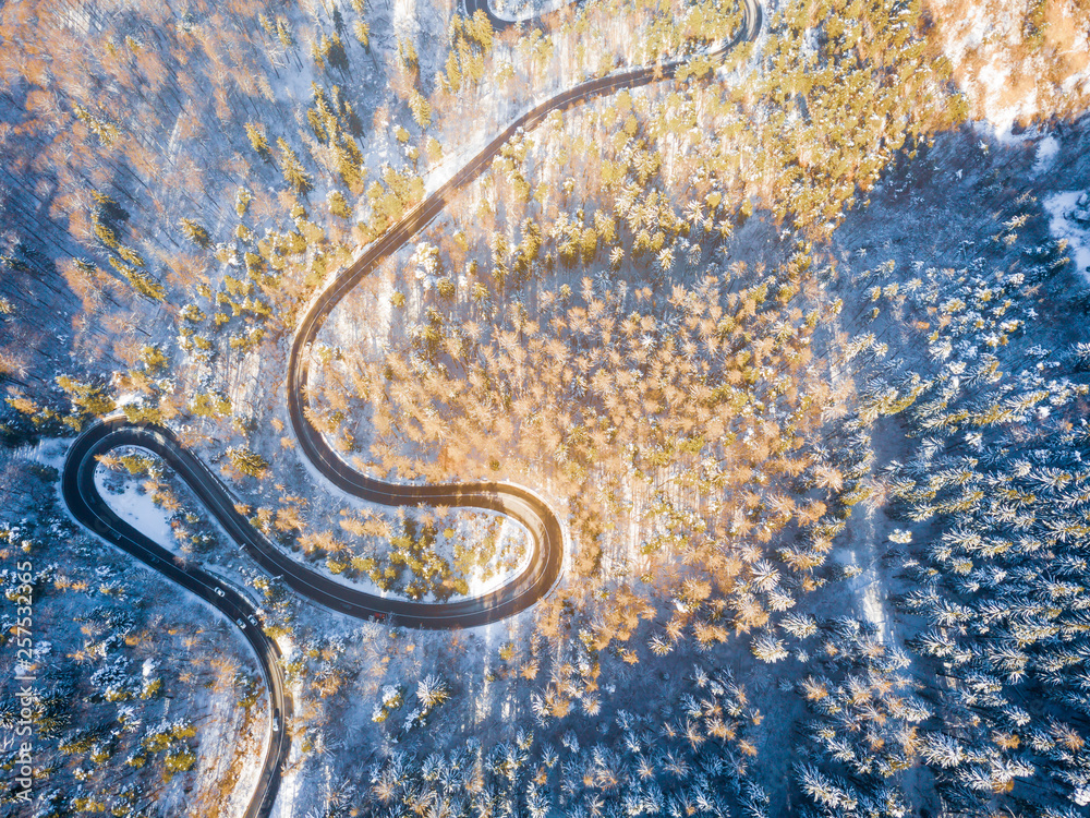 Winding road through the forest, from high mountain pass, in winter time. Aerial view by drone . Romania