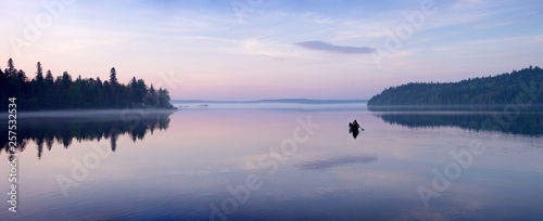 A man paddling a canoe at dawn on Allagash Lake