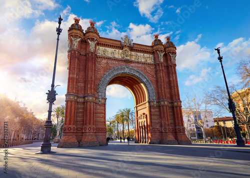 Sunrise at Triumphal Arch in Barcelona, Catalonia, Spain. Arc de Triomf at boulevard street. Alley with tropical palm trees. Early morning landscape with shadows and blue sky with clouds. Famous.