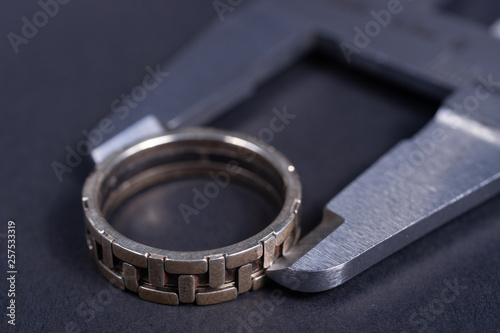 Vintage steel caliper measuring sterling silver male ring closeup. Ring in focus. Tool in very good condition. Stock photo on blurred gray background.