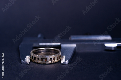 Vintage steel caliper measuring sterling silver male ring closeup. Ring in focus. Tool in very good condition. Stock photo on blurred gray background.