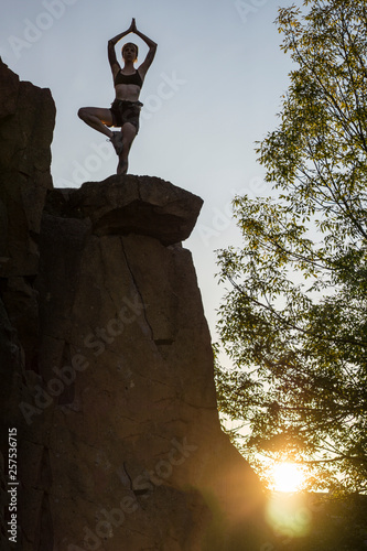 Silhouetted rock climbers on top of rock wall in lotus position photo