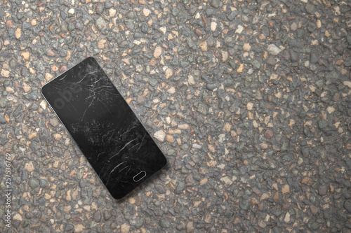 smartphone with a crashed and dirty screen on asphalt