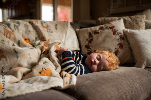 young boy sleeping on couch at home under warm blanket