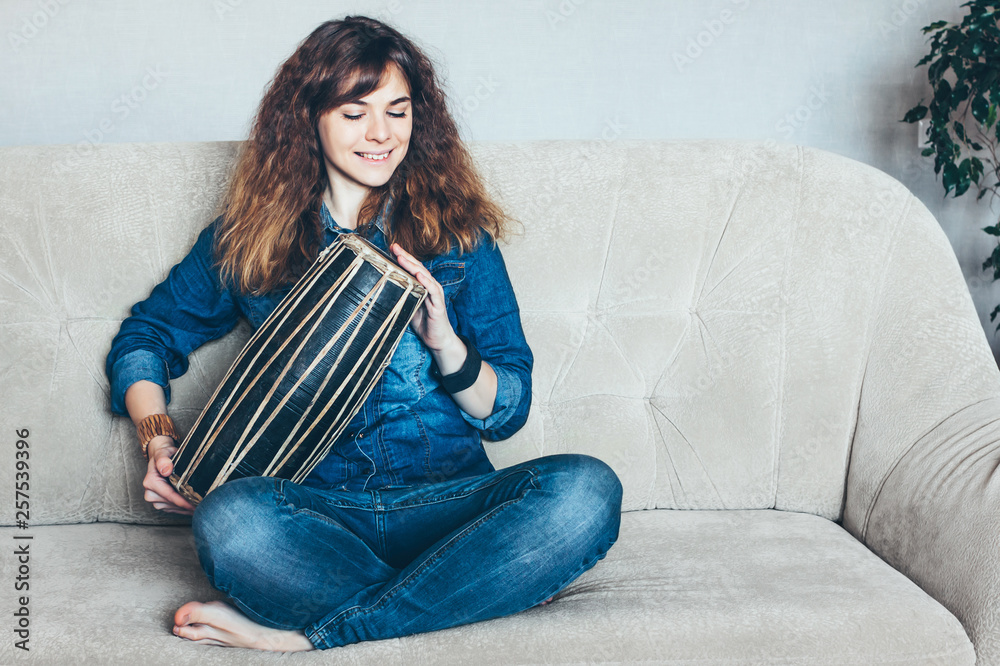 Obraz premium Young woman playing ethnic indian hand drum mridangam at home.