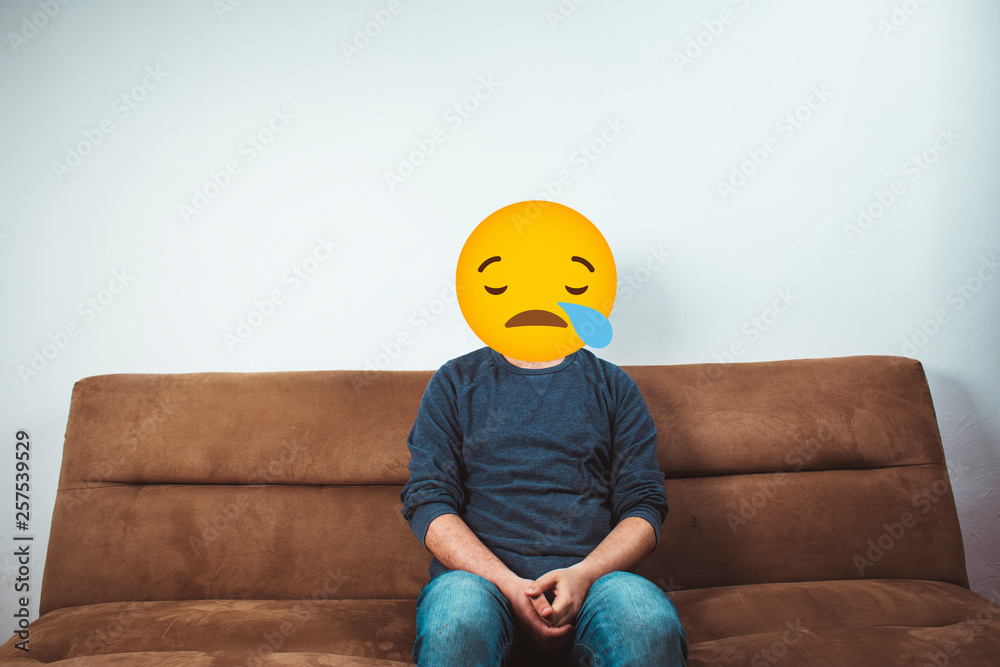 view of a man sitting alone on sofa with a Sad face emoji Stock Photo |  Adobe Stock