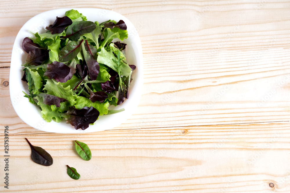 Plate with lettuce on a wooden background. Salad greens. Organic food. Food For Vegans. Design a banner with natural food. Salad to lose weight. Flat lay, top view. Plate with lettuce on a wooden background. Salad greens. Organic food. Food For Vegans. Design a banner with natural food. Salad to lose weight. Flat lay, top view.