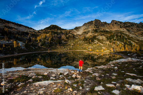 A young man walks next to an alpine lake beneath steep mountains of the Cascades in the Pasayten Wilderness in Washington. photo