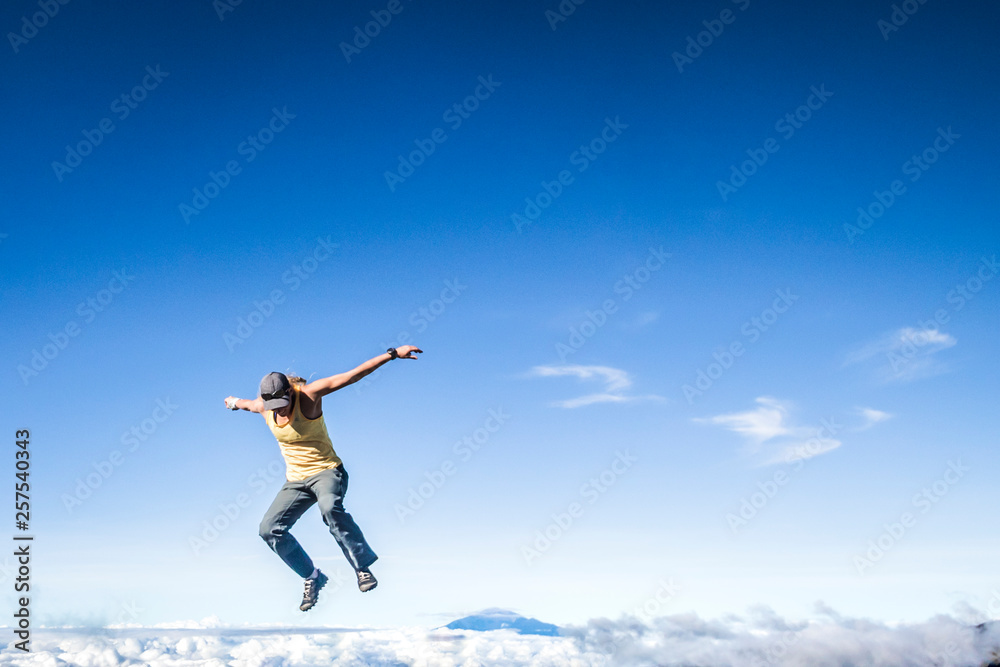 Woman jumping with clouds and mountain peak in background Woman jumping with clouds and mountain peak in background