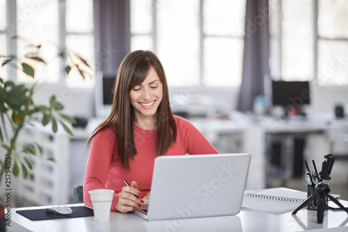 Beautiful smiling Caucasian businesswoman sitting in modern office and using laptop.