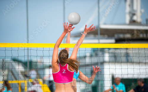 An athletic woman jumping to make wall block at beach volleyball net. Stretched arms and open hands to defend