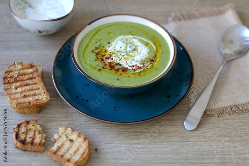 Creamy vegetable soup with kale, cabbage, celery and millet, decorated with olive oil, yoghurt sauce and chilli flakes. Served with toasted bread and lemony yoghurt sauce. Selective focus.