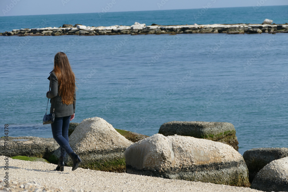 Giovane donna che passeggia in riva al mare in una bella giornata di primavera