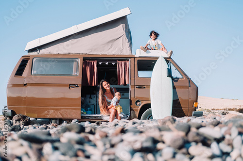 Mother with children by vintage camper van on stony beach photo