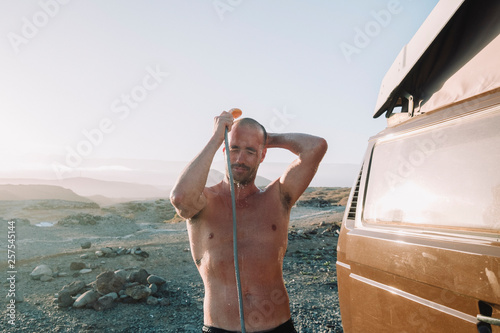 Man taking shower out of his van on rocky beach photo