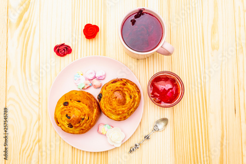 Karkade tea from hibiscus petals (Sudanese rose). Gentle romantic breakfast concept. Buns, meringues, strawberry jelly. On a wooden background, top view.