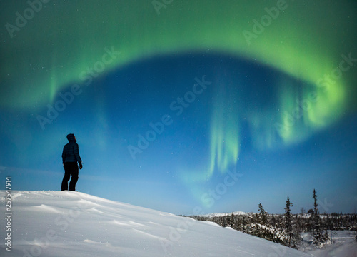 Silhouette of man standing on the mountain looking at Aurora Borealis photo