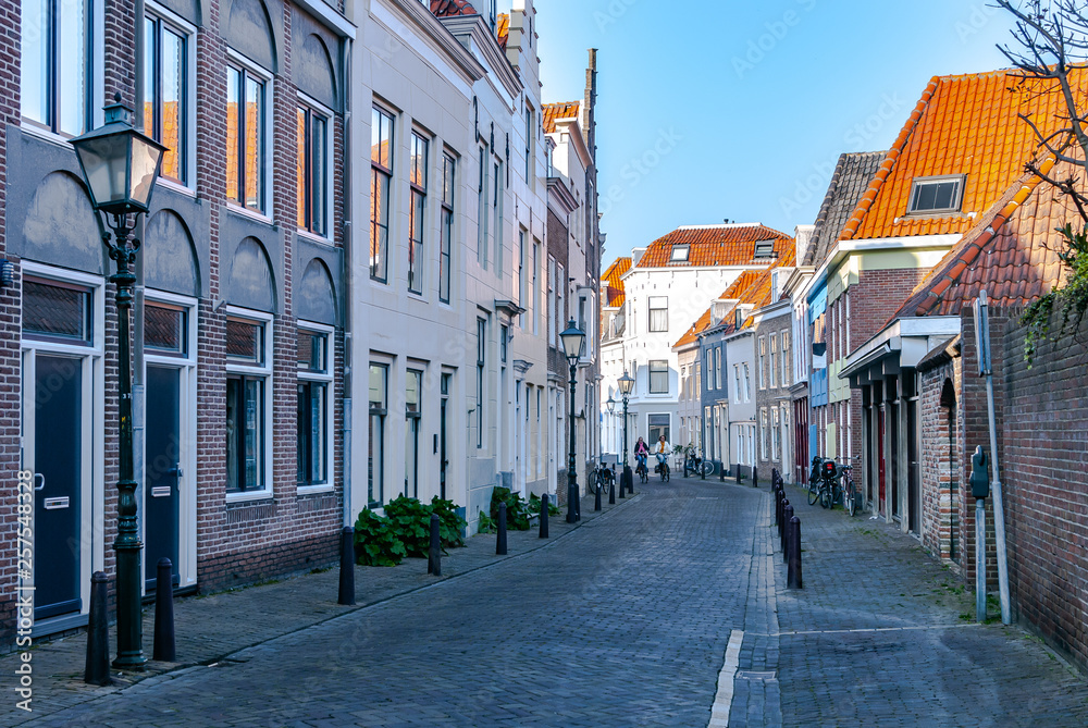 A street view with picturesque historical houses, old lanterns and two approaching cycling ladies on the other end of the street. .Outdoor activities. Bicycling. Travel concept. Vacation. Day off.