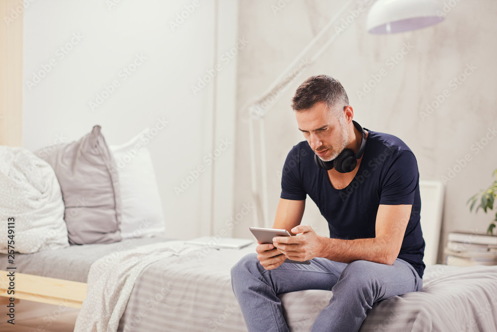 Caucasian man in forties sitting on bed in bedroom and using tablet. Caucasian man in forties sitting on bed in bedroom and using tablet.