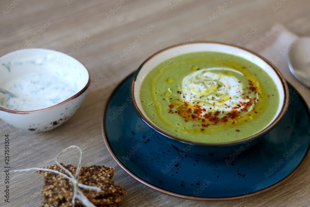 Creamy vegetable soup with kale, cabbage, celery and millet, decorated with olive oil, yoghurt sauce and chilli flakes. Served with seed crackers and lemony yoghurt sauce. Selective focus.