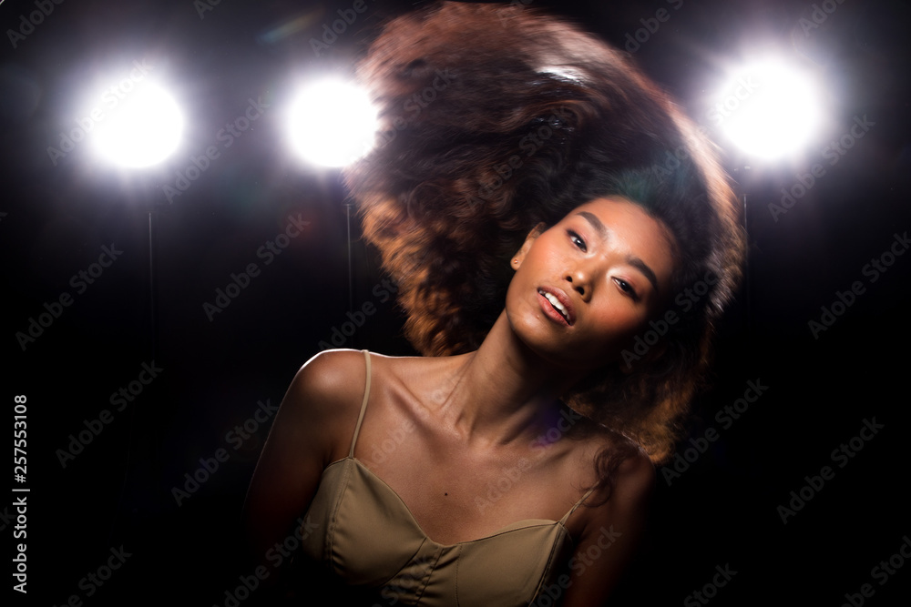 Fashion Young Asian Woman Tan skin eyes beautiful make up fashion dress throw flying hair in air blur motion. Studio Lighting Dark Background smoke fog back rim light low exposure