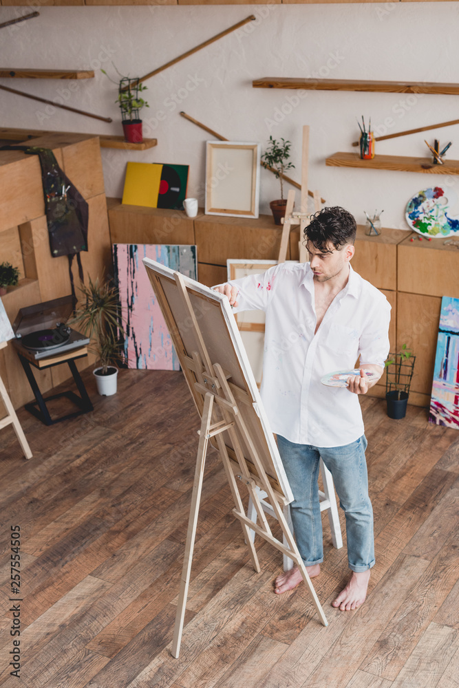 handsome artist in white shirt and blue jeans painting on canvas in painting studio