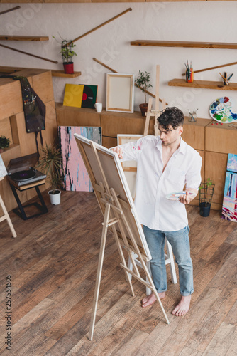 handsome artist in white shirt and blue jeans painting on canvas in painting studio © LIGHTFIELD STUDIOS