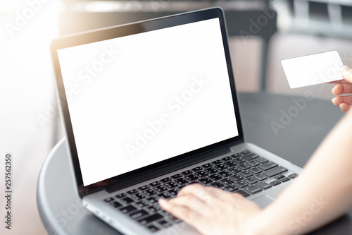 Mockup image of a businesswoman using laptop with blank white desktop screen and blank credit cards with coffee cup on wooden table in cafe