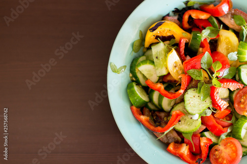 fresh vegetable salad with red pepper cucumber tomato and basil on blue plate on wooden background