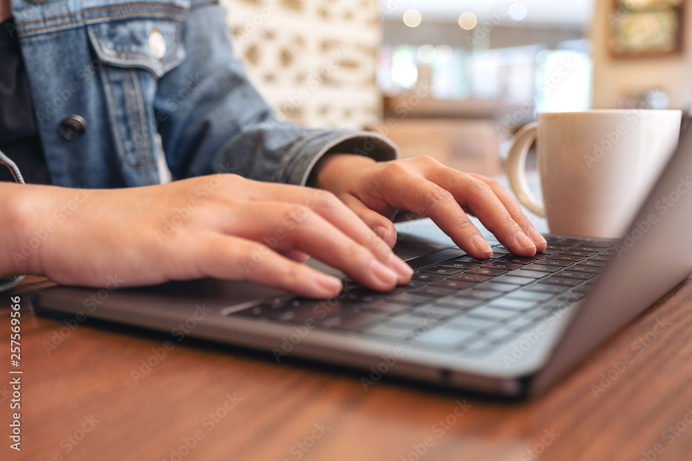 Closeup image of woman's hands using and typing on laptop computer keyboard with coffee cup on the table Closeup image of woman's hands using and typing on laptop computer keyboard with coffee cup on the table