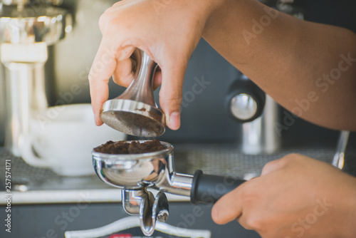 Barista tamping coffee with coffee machine background