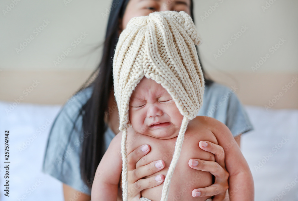 Φωτογραφία Close-up of choleric infant baby boy wear some knit clothes in the bedroom holding by mother